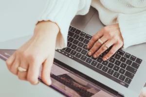 Fashion designer's hands typing on laptop keyboard using tech pack software tool.